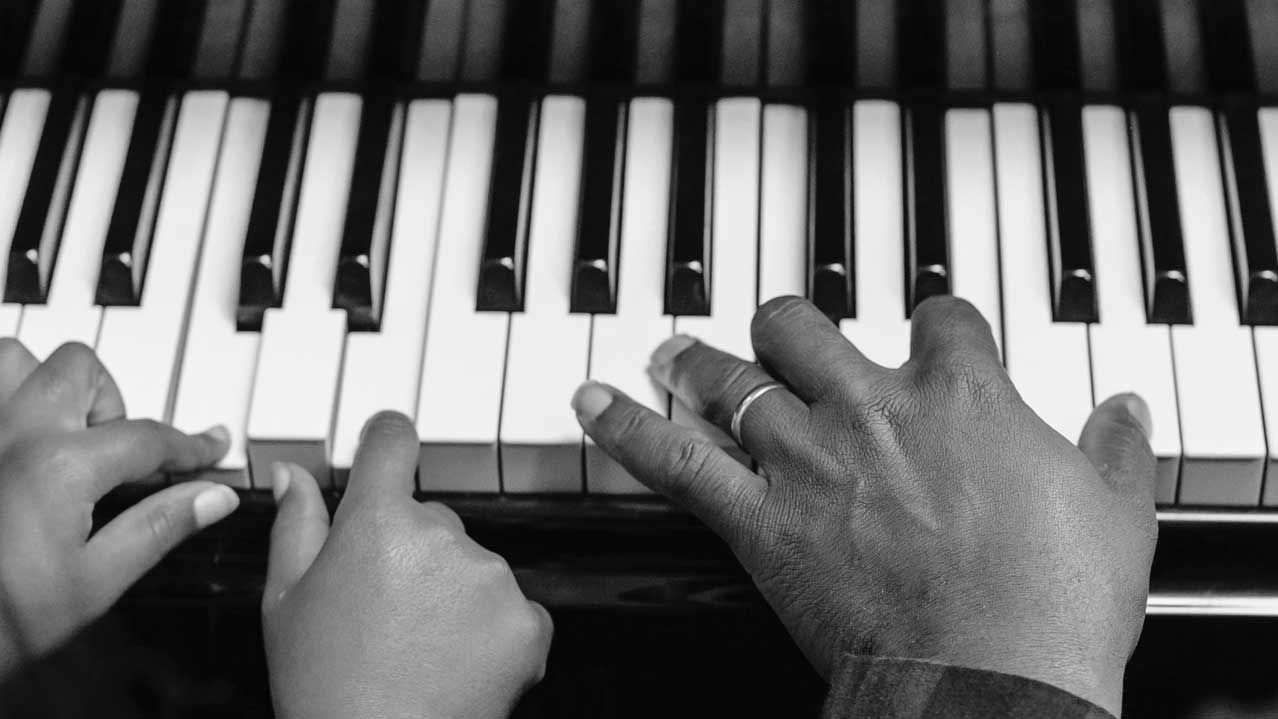 Young childs hand and adults hand playing the keys on the piano